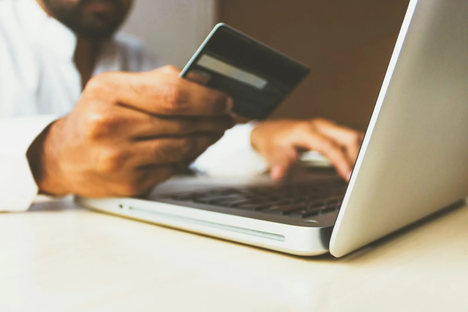 Person holding a payment card while using a laptop at a desk