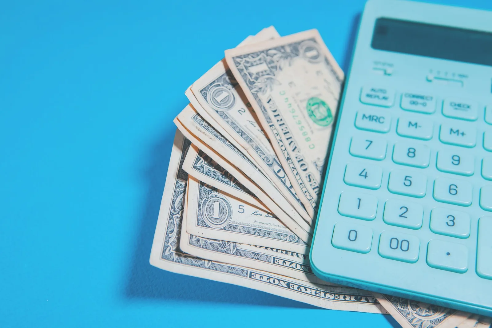 U.S. dollar bills beside a calculator on a bright blue surface
