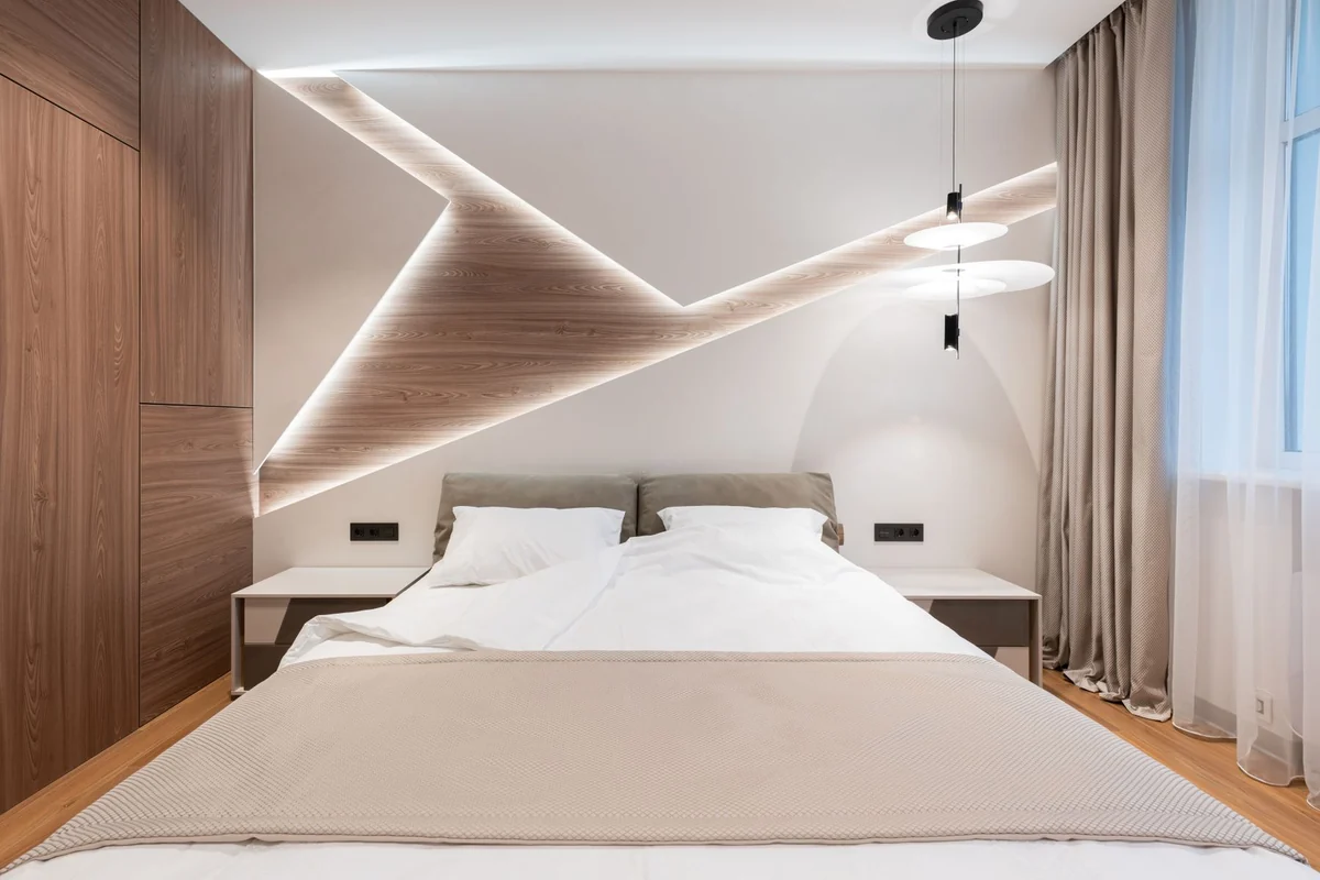 Bright hotel guestroom with a white double bed, wood paneling, pendant lights, and a curtained window.