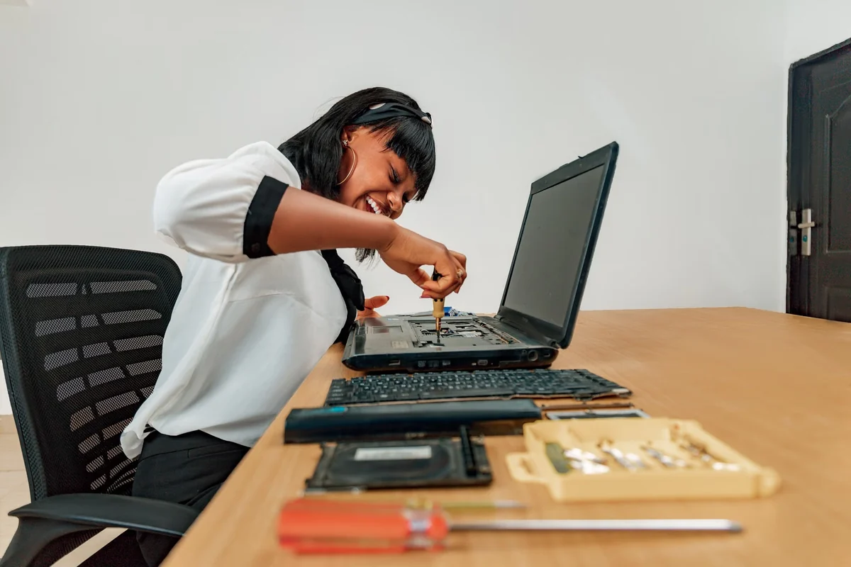Technician using a screwdriver on an opened laptop, with its removed keyboard and repair tools on the desk.